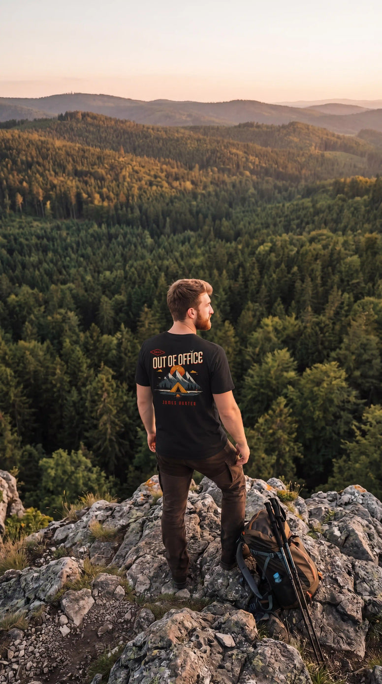 Man standing on a rocky outcrop overlooking a forested valley with a sunset.