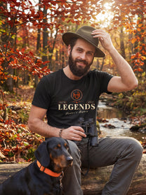 Man wearing a black t-shirt with 'Legends' text and a logo, sitting with a dog in an autumn forest.