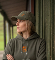 Person wearing a green hoodie and cap with a logo, standing outdoors.