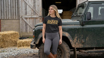 Woman wearing a 'James Hunter' shirt standing next to a green jeep in a rural setting.