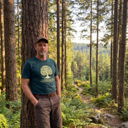 Man in forest wearing eco-friendly Evergreen T-shirt, nature apparel for outdoor adventures and sustainability.